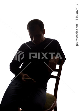 Young man sits with a mobile phone in hand - silhouette 110382397