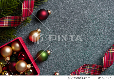An assortment of Christmas baubles with a tartan ribbon on a glittery grey background, festive holiday concept. An assortment of Christmas baubles with a tartan ribbon on a glittery grey background, festive holiday concept. 110382476