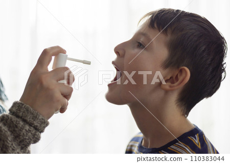 The child receives medication through a mouth spray for a sore throat 110383044