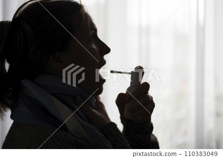 A woman with a sore throat sprays a medicinal aerosol spray down her throat 110383049