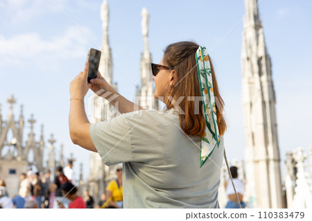 Beautiful 30s woman taking selfie on Roof of Milan Cathedral Duomo di Milano, Italy. Traveling Europe in summer. Attractive female is exploring city, tourist makes photo or video on smartphone 110383479