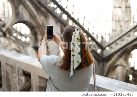 Beautiful 30s woman taking selfie on Roof of Milan Cathedral Duomo di Milano, Italy. Traveling Europe in summer. Attractive female is exploring city, tourist makes photo or video on smartphone Beautiful 30s woman taking selfie on Roof of Milan Cathedral Duomo di Milano, Italy. Traveling Europe in summer. Attractive female is exploring city, tourist makes photo or video on smartphone 110383485