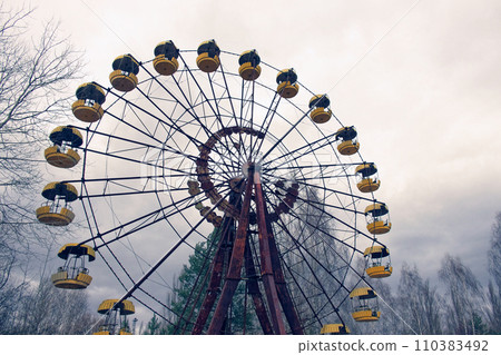 An old Ferris wheel with yellow gondolas, surrounded by trees. 110383492