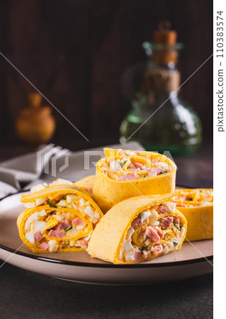 Tortilla rolls with salad of sausages, eggs, cheese and herbs on a plate vertical view 110383574