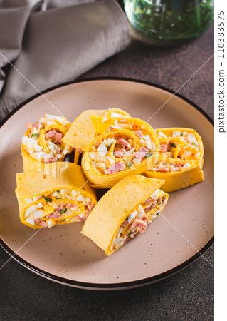 Mini tortilla rolls with chopped sausages, cheese, eggs and herbs on a plate vertical view Mini tortilla rolls with chopped sausages, cheese, eggs and herbs on a plate vertical view 110383575