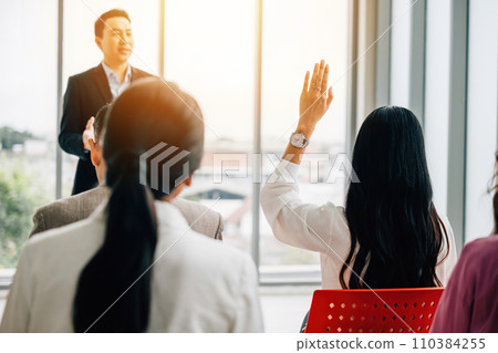 A diverse crowd in a corporate event raises their hands for questions, voting, or volunteering, emphasizing teamwork and audience interaction during the conference. 110384255