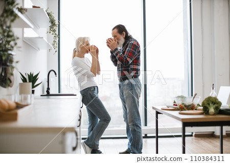 Wife and husband with gray beard drinking hot drinks from mugs. 110384311