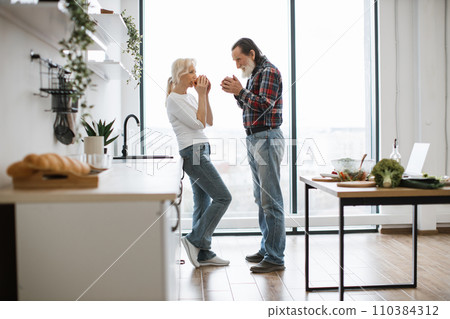 Wife and husband with gray beard drinking hot drinks from mugs. 110384312