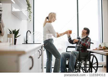 Pensioners wife and husband in wheelchair drinking hot drinks from mugs 110384313