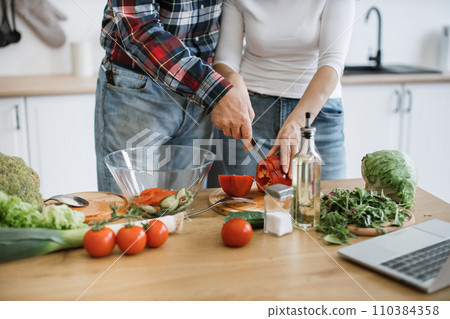 Cropped view of hands of retired couple cutting pepper while holding knife together in hands 110384358