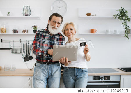 Happy elderly husband and wife holding laptop and credit card paying for food. Happy elderly husband and wife holding laptop and credit card paying for food. 110384945