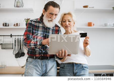Happy elderly husband and wife holding laptop and credit card paying for food. Happy elderly husband and wife holding laptop and credit card paying for food. 110384946