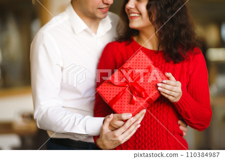 A young man gives his beloved a present and closes her eyes with a hand. Valentine's Day. 110384987
