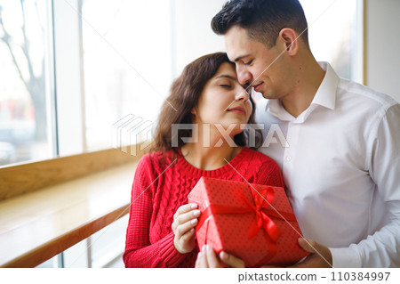 A young man gives his beloved a present and closes her eyes with a hand. Valentine's Day. A young man gives his beloved a present and closes her eyes with a hand. Valentine's Day. 110384997