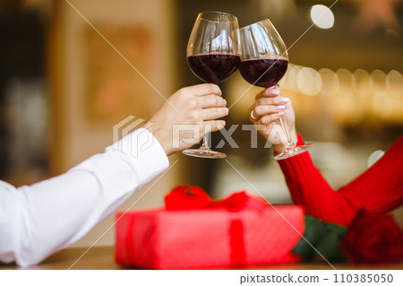 Couple clink glasses with red wine. Lovers give each other gifts. Lovely romantic dinner. Couple clink glasses with red wine. Lovers give each other gifts. Lovely romantic dinner. 110385050