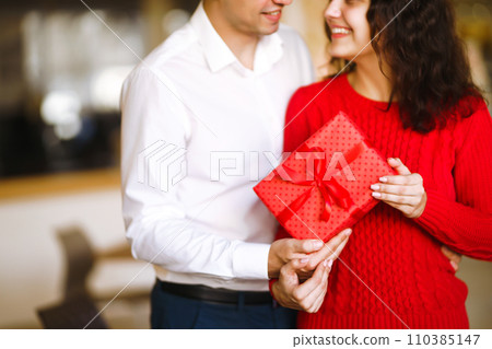 Man gives to his woman a gift box with red ribbon. Valentine's Day, holiday and surprise concept. Man gives to his woman a gift box with red ribbon. Valentine's Day, holiday and surprise concept. 110385147