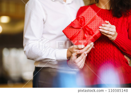 Man gives to his woman a gift box with red ribbon. Valentine's Day, holiday and surprise concept. Man gives to his woman a gift box with red ribbon. Valentine's Day, holiday and surprise concept. 110385148