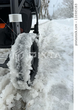 Close-up of wheels of baby carriage covered with snow. Difficult traffic in streets on snowy winter Close-up of wheels of baby carriage covered with snow. Difficult traffic in streets on snowy winter 110385163