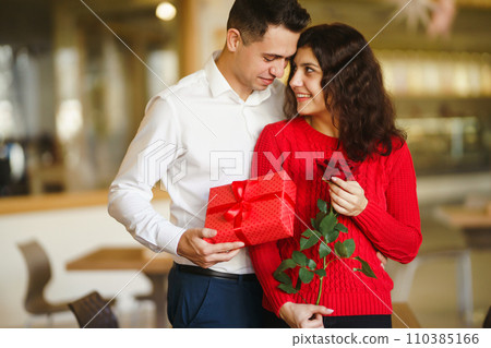 Man gives to his woman a gift box with red ribbon. A loving couple celebrating Valentine's Day. 110385166