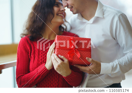 Man gives to his woman a gift box with red ribbon. A loving couple celebrating Valentine's Day. 110385174