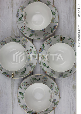 Top view of a porcelain tea set with flowers on a white table. Utensils for preparing hot drinks Top view of a porcelain tea set with flowers on a white table. Utensils for preparing hot drinks 110385192