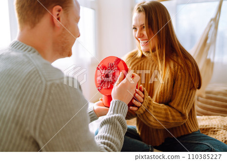 Valentine's Day concept. Exchange of gifts. Young couple at home celebrating Valentine's Day. Valentine's Day concept. Exchange of gifts. Young couple at home celebrating Valentine's Day. 110385227