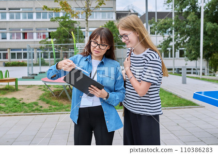Talking teacher and teenage schoolgirl outdoor, school building background Talking teacher and teenage schoolgirl outdoor, school building background 110386283