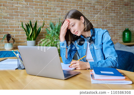 Sad tired female college student at home at her desk with laptop and textbooks 110386308