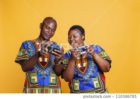 Happy couple playing online game on smartphones, having fun leisure activity together. Wife looking at husband mobile phone screen and checking videogame progress Happy couple playing online game on smartphones, having fun leisure activity together. Wife looking at husband mobile phone screen and checking videogame progress 110386785