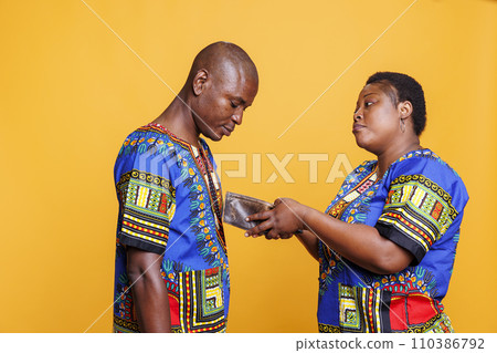 Frustrated african american woman showing empty wallet to sad husband. Displeased poor black couple wearing ethnic clothes having bankruptcy problem and financial difficulties 110386792