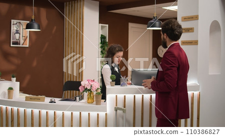 Businessman shows id info in lobby, using documents for check in before important conference attendance. Front desk employee reviewing passport at reception, offering good services to guest. 110386827