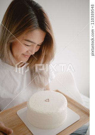 Beautiful woman looking at her surprised minimal white cake with happiness on her special day. 110389548