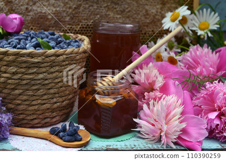 Still life with natural honey, honeycomb cut in pieces and honeysuckle berry with flowers on wooden background outside. Countryside summer rural background, vintage concept, healthy food 110390259