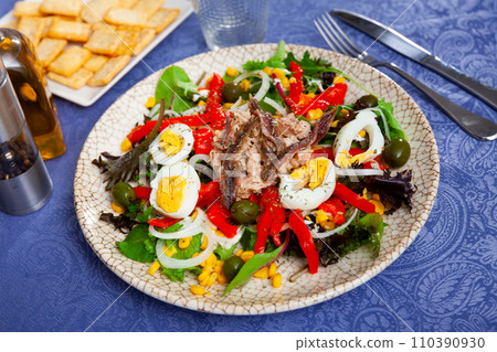 Corn, olive, anchovy, pepper, lettuce salad served on plate 110390930