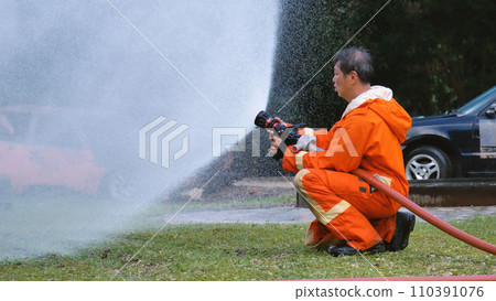 Firefighter Rescue team training in fire fighting extinguisher. Firefighter teamwork fighting with flame using fire hose chemical water foam spray engine. Fireman wear hard hat, safety suit uniform 110391076