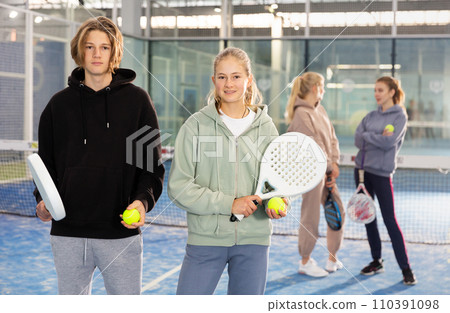 Portrait of two teenage tennis players standing holding padel rackets and balls 110391098