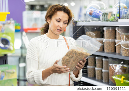 Female shopper selecting dry pelleted food for turtles in pet store 110391211
