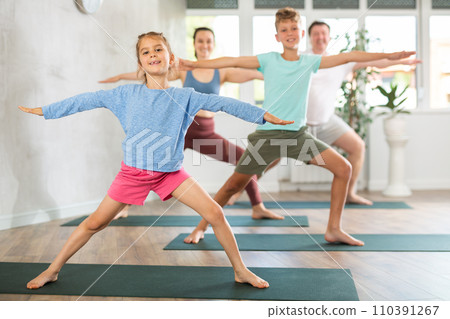 Pleasant little girl practicing warrior pose of yoga with her family 110391267