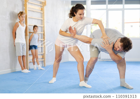 Woman practicing armlock in training bout with husband during family self defence course Woman practicing armlock in training bout with husband during family self defence course 110391313