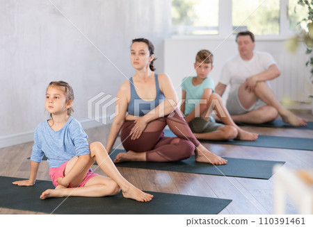 Little girl performs Lord of fish Ardha Matsyendrasana asana, family in background Little girl performs Lord of fish Ardha Matsyendrasana asana, family in background 110391461