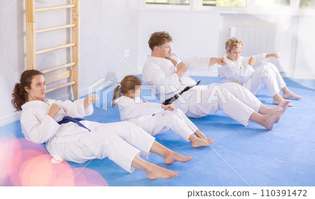 Tweens with parents in kimonos practicing abdominal crunches with punches 110391472