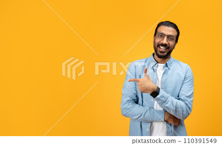 A charismatic man with a beard and glasses smiles and points sideways with his left hand 110391549