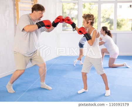 Preteen boy practicing boxing punches in sparring with father in gym 110391579