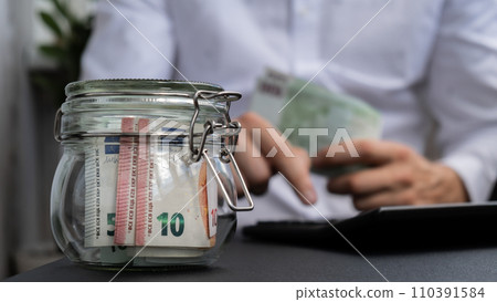 Man hands counting expenses banknotes of euro cash from glass jar in the piggy bank on calculator. Close up of hands unrecognizable Businessman. Save up budget investment concept. Euros fund savings 110391584