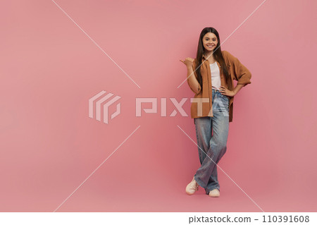 Cheerful teenage girl pointing to the side with thumb up Cheerful teenage girl pointing to the side with thumb up 110391608