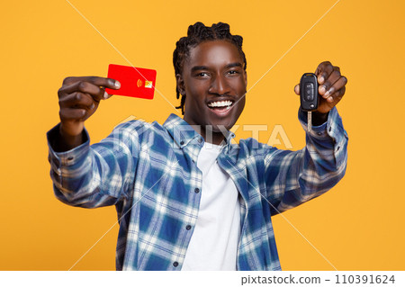 Smiling young black man showing credit card and car keys 110391624