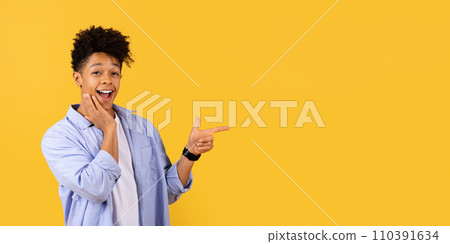 Surprised young black man pointing aside at free space on yellow background Surprised young black man pointing aside at free space on yellow background 110391634