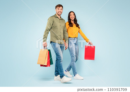 Smiling couple walking with shopping bags on blue background Smiling couple walking with shopping bags on blue background 110391709