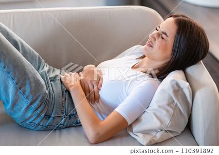 Lady suffering from abdominal discomfort, having painful menstruation cramps indoors Lady suffering from abdominal discomfort, having painful menstruation cramps indoors 110391892