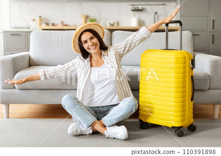 Excited woman in straw hat, sitting with arms wide open beside suitcase Excited woman in straw hat, sitting with arms wide open beside suitcase 110391898